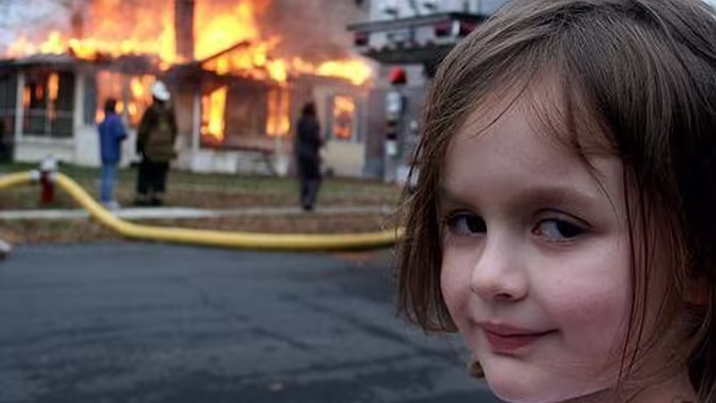 Zoë Roth as Disaster Girl smiling in front of a controlled house fire